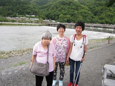 京都の渡月橋を背景に笑顔を見せる利用者３人の写真