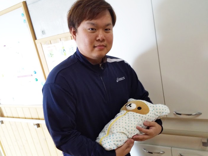Ｗ氏が赤ちゃんをイメージしてクマのぬいぐるみを抱いている写真