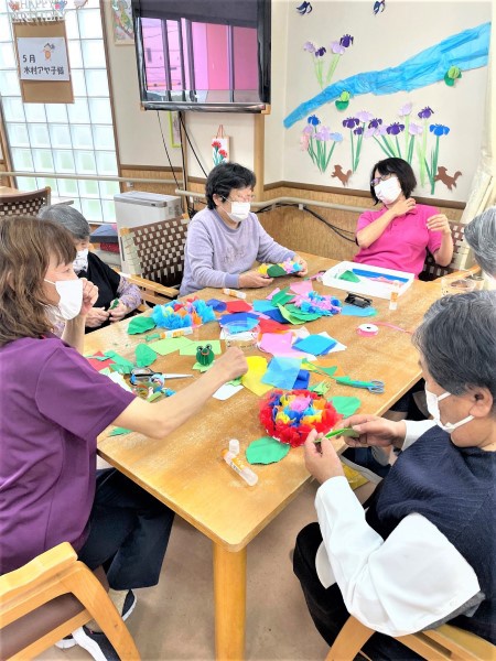 利用者さんと職員でテーブルを囲み、折り紙で飾り物を作っている様子
