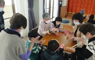 認知症カフェ参加者と地域の学童の子どもたちがあやとりで遊んでいる写真です